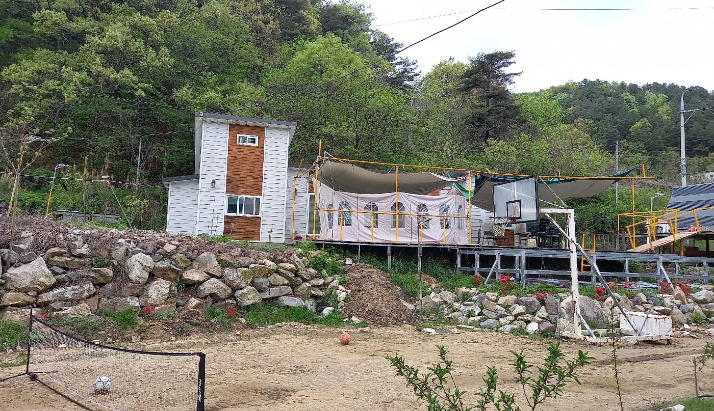 목조주택과 천막 식사 공간, 돌 축대가 보이는 농장 전경