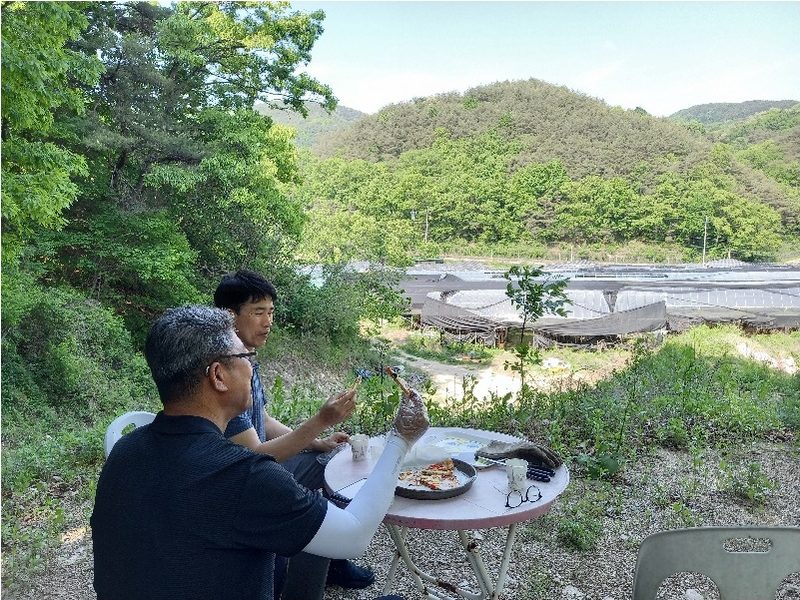 산과 재배사가 보이는 자리에서 둘러앉아 식사하는 모습